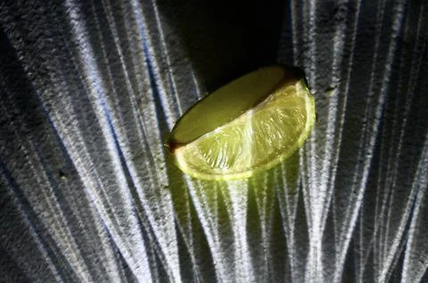 Fresh Lime Wedge with Dramatic Glass Refraction Shadows on Dark Surface 写真素材