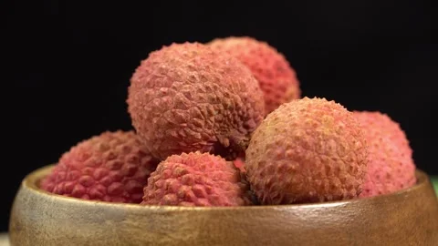 Fresh lychee fruit in shell rotate in wooden bowl in macro on black background. Stock-Footage 244811184
