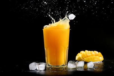 Fresh mango juice. A splash of mango cocktail on a black background. Ice cubes Photos
