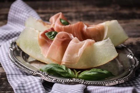 Fresh Melon with Prosciutto and Basil on vintage wooden background Stock Photos