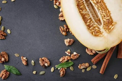 Fresh melon with walnuts and cinnamon sticks on dark surface Stock Photos