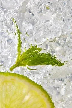 Fresh mint leaf and a slice of lime with bubbles in a glass with ice. Macro.. Stock Photos