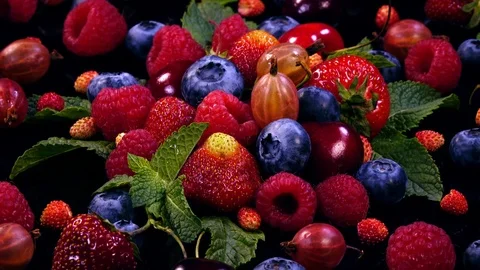 Fresh mixed juicy berries and mint leaves on black background in 4K Stock Footage