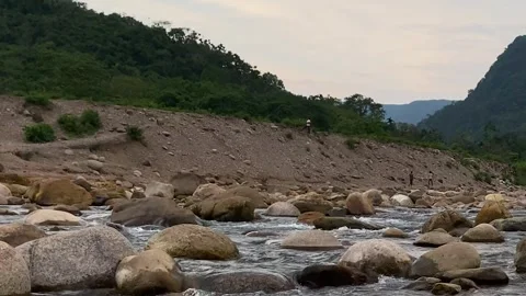 Fresh mountain water flows across river rocks beneath hills of Sylhet Stockbeeldmateriaal 335026302