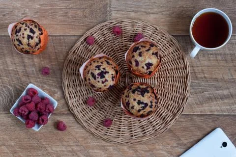 Fresh muffins with raspberry, cup of tea and smartphone on a wooden desk. Stock Photos