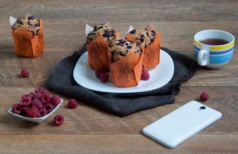 Fresh muffins with raspberry, cup of tea and smartphone. Stock Photos