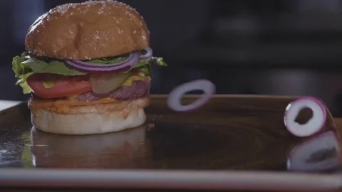 Fresh onion circles falling down on hamburger, slow motion, junk food concept. Stock Footage 80603463