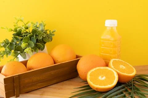 Fresh oranges and juice bottle on wood table with green plant and palm leaf in Stock Photos