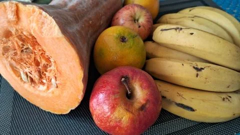 Fresh organic pumpkin and assorted fruits arranged on dark matting Stock Photos