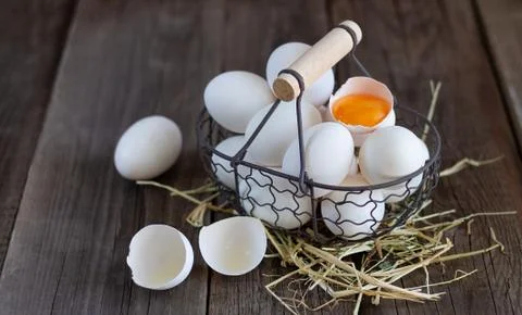 Fresh organic white eggs with eggshell and yolk in metal mesh basket on straw Stock Photos