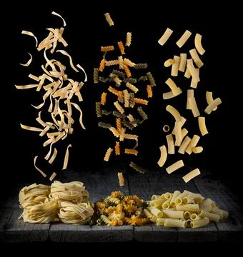 Fresh pasta falling in different shapes and colours on a wood in front of a.. Stock Photos