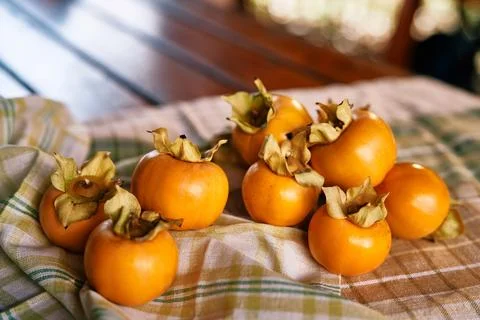 Fresh persimmons on a checkered cloth with a rustic wooden background. Stock Photos