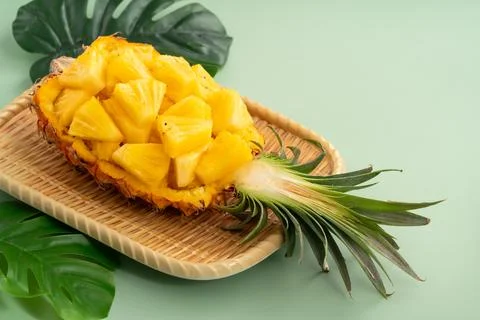Fresh pineapple chunks served in a pineapple bowl on green table background. Stock Photos