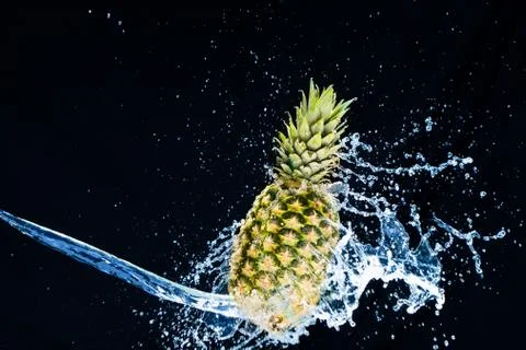 Fresh pineapple gets splashed with water on black background. Concept of summ Foto stock
