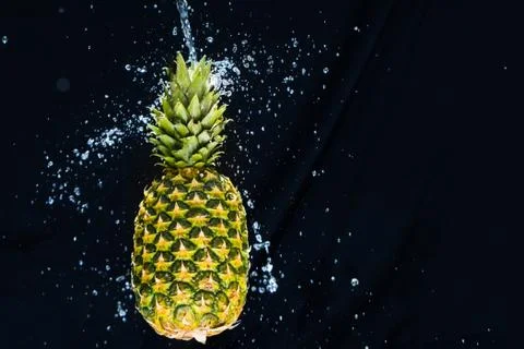 Fresh pineapple gets splashed with water on black background. Concept of summ Foto stock