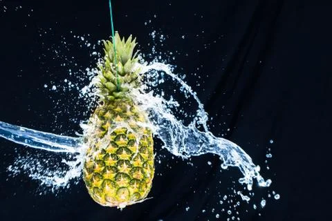 Fresh pineapple gets splashed with water on black background. Concept of summ Foto stock