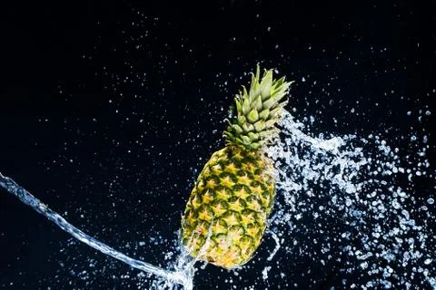 Fresh pineapple gets splashed with water on black background. Concept of summ Foto stock