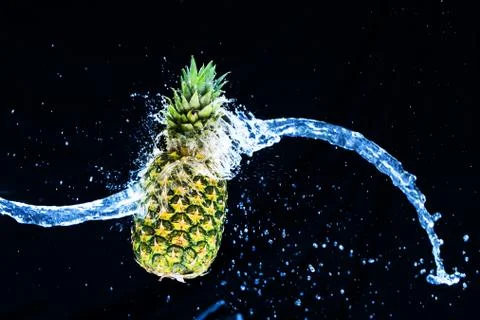 Fresh pineapple gets splashed with water on black background. Concept of summ Foto stock
