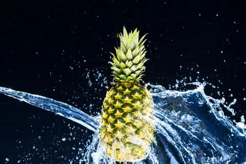 Fresh pineapple gets splashed with water on black background. Concept of summ Stock Photos