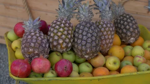 Fresh pineapples and apples arranged in wheelbarrow at market stand, warm Stock-Footage 321817259