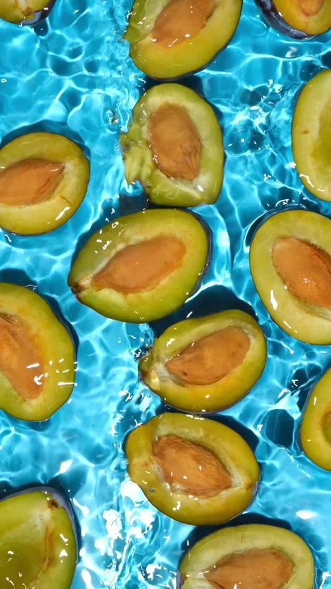 Fresh plum halves with pits floating in clean water overhead view. Stock Footage 346204516
