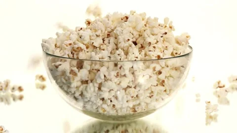 Fresh popcorn falling into a clear glass bowl slowly Video stock 333835743
