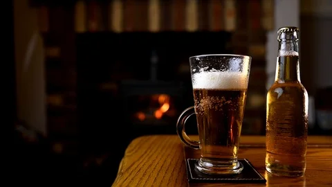 Fresh poured beer on oak table infront of fireplace at home Video stock 127544981
