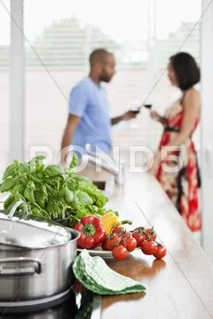 Fresh produce on a kitchen counter and a young couple in background Stock Photos