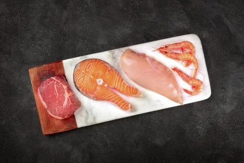 Fresh proteins. Raw beef meat, salmon fish, chicken breast, and shrimps, shot Stock Photos
