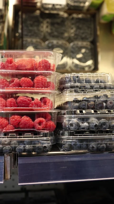 Fresh raspberries and blueberries packed in clear containers at grocery store Stock Footage 345978596