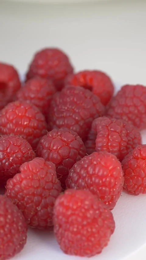 Fresh raspberries rotating on white surface represent minimalist food aesthetics Stock Footage 333116892