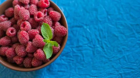 Fresh raspberry in ceramic bowl on the blue background Stock Photos