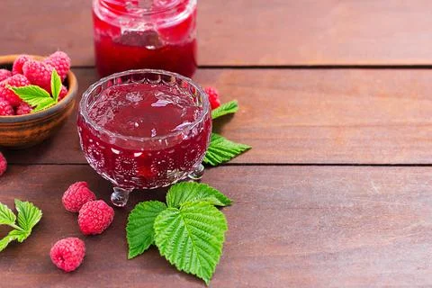 Fresh raspberry jam in a glass jar on a wooden table, next to fresh raspberri Stock Photos