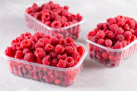 Fresh raspberry in plastic boxes on light background Stock Photos
