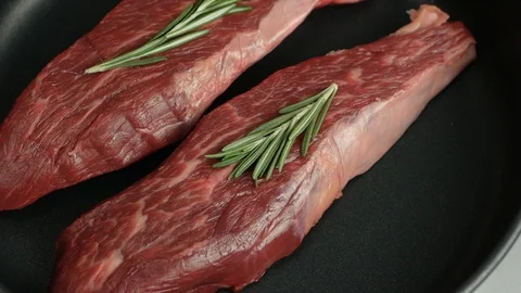 Fresh raw beef steak with rosemary and pepper rotating on a frying pan Stock Footage 128458396