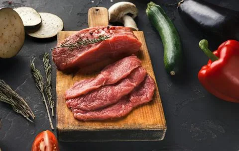 Fresh raw beef steak slices on wooden cutting board with vegetables Stock Photos