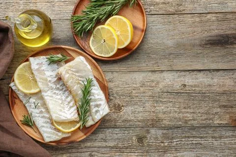 Fresh raw cod fillets with rosemary, lemon and oil on wooden table, flat la.. Stock Photos