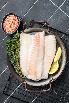 Fresh raw cod fish fillets with herbs served on steel tray. Black backgroun.. 스톡 사진
