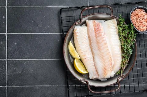 Fresh raw cod fish fillets with herbs served on steel tray. Black backgroun.. 스톡 사진