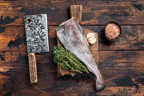 Fresh Raw cod or codfish fish on wooden board with cleaver. Dark Wooden Stock Photos