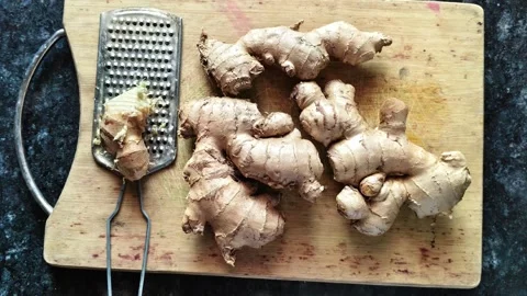 Fresh raw ginger roots and a metal grater on a wooden cutting board Видео 326988585