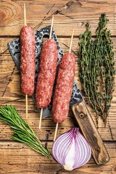 Fresh Raw kofta or lula kebabs skewers on a butcher cleaver with herbs. wooden Stock Photos
