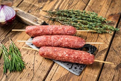 Fresh Raw kofta or lula kebabs skewers on a butcher cleaver with herbs. wooden Stock Photos