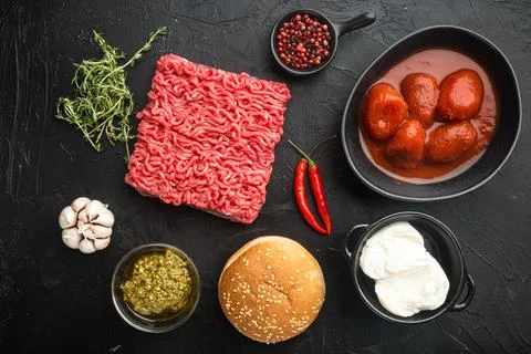 Fresh raw minced beef steak burgers with spices ingredients, on black stone b Foto stock