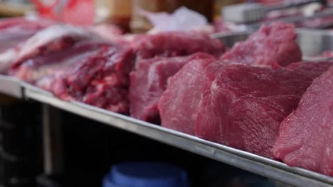 Fresh raw pork pieces placed on a metal tray at a butcher stall where large Vídeos de archivo 332300866