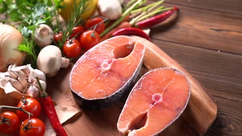 Fresh raw salmon fish steak with herbs and vegetables on wooden background Видео 145185750