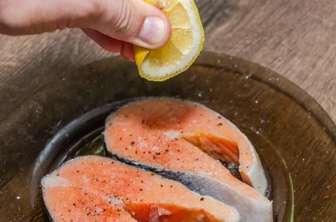 Fresh raw salmon fish steaks on a plate, the cook pours lemon on them Stock Photos