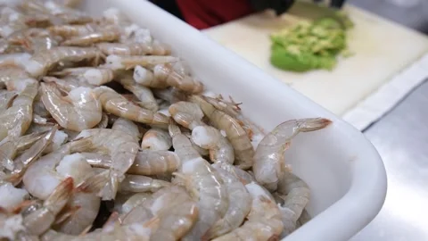 Fresh raw shrimp in foreground with chef cutting avocado in commercial kitchen Stock Footage 339864256