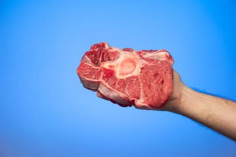 Fresh raw slice of red beef shank held in hand by Caucasian male hand isolate Stock-Fotos