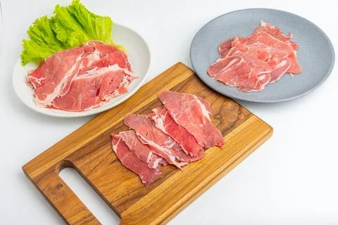 Fresh raw sliced beef meat on wooden board and plate with green lettuce iso.. Stock Photos